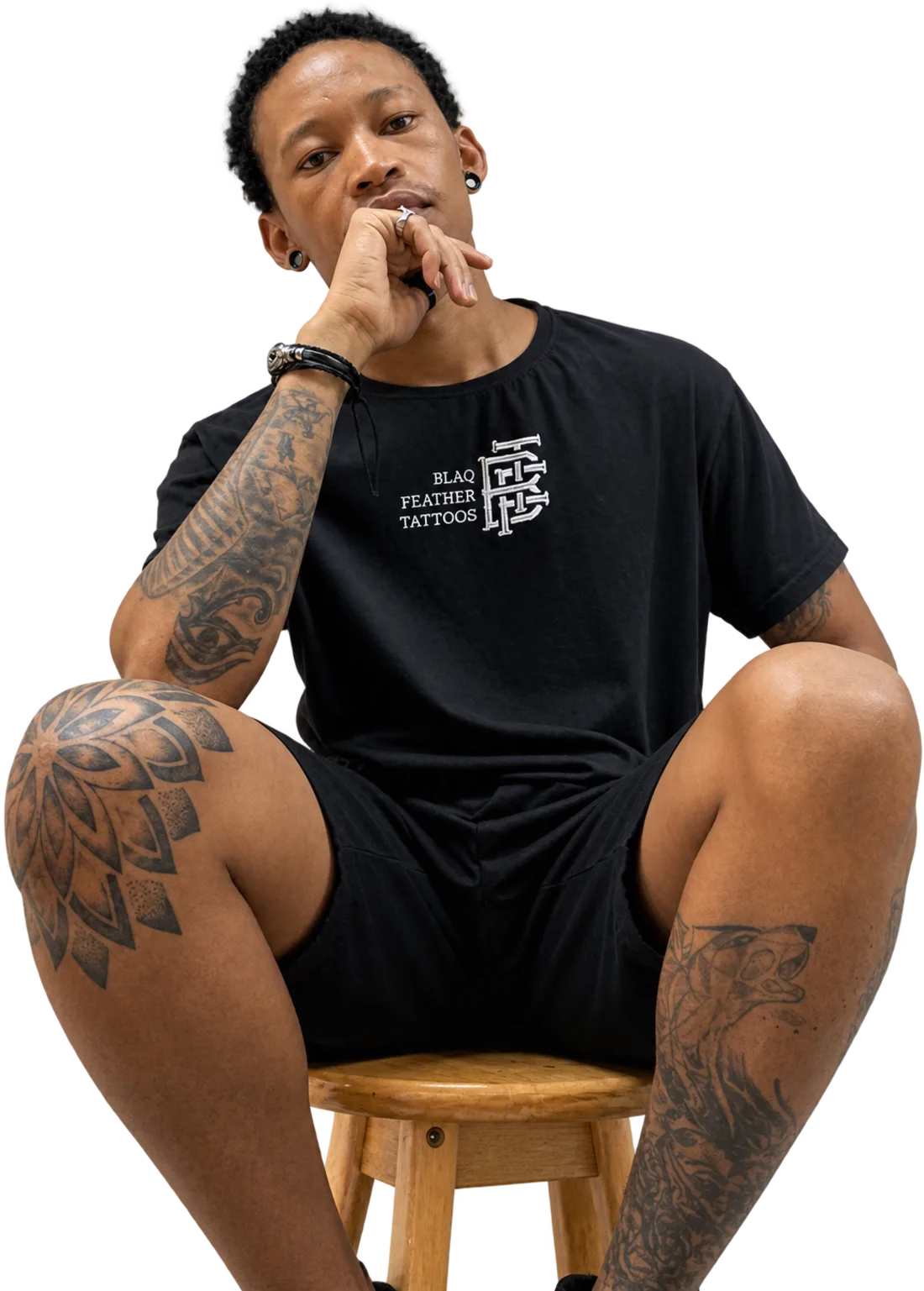 Payne, head artist at BlaQ Feather, seated on a stool