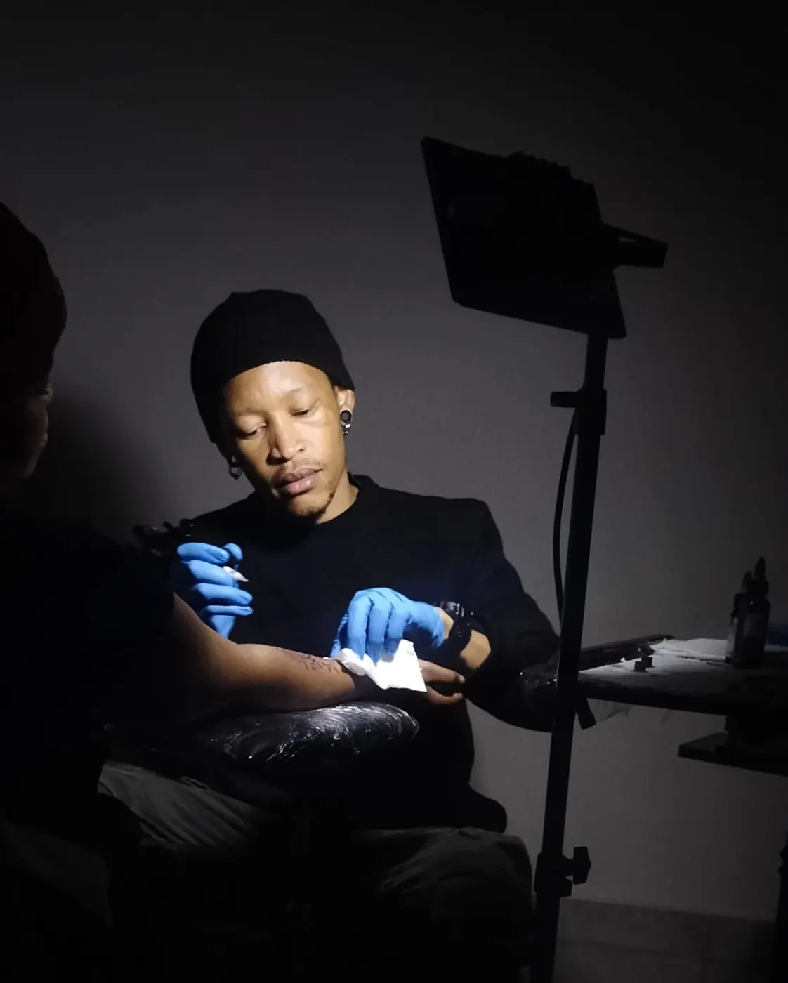 Payne tattooing in a dark room under a single light